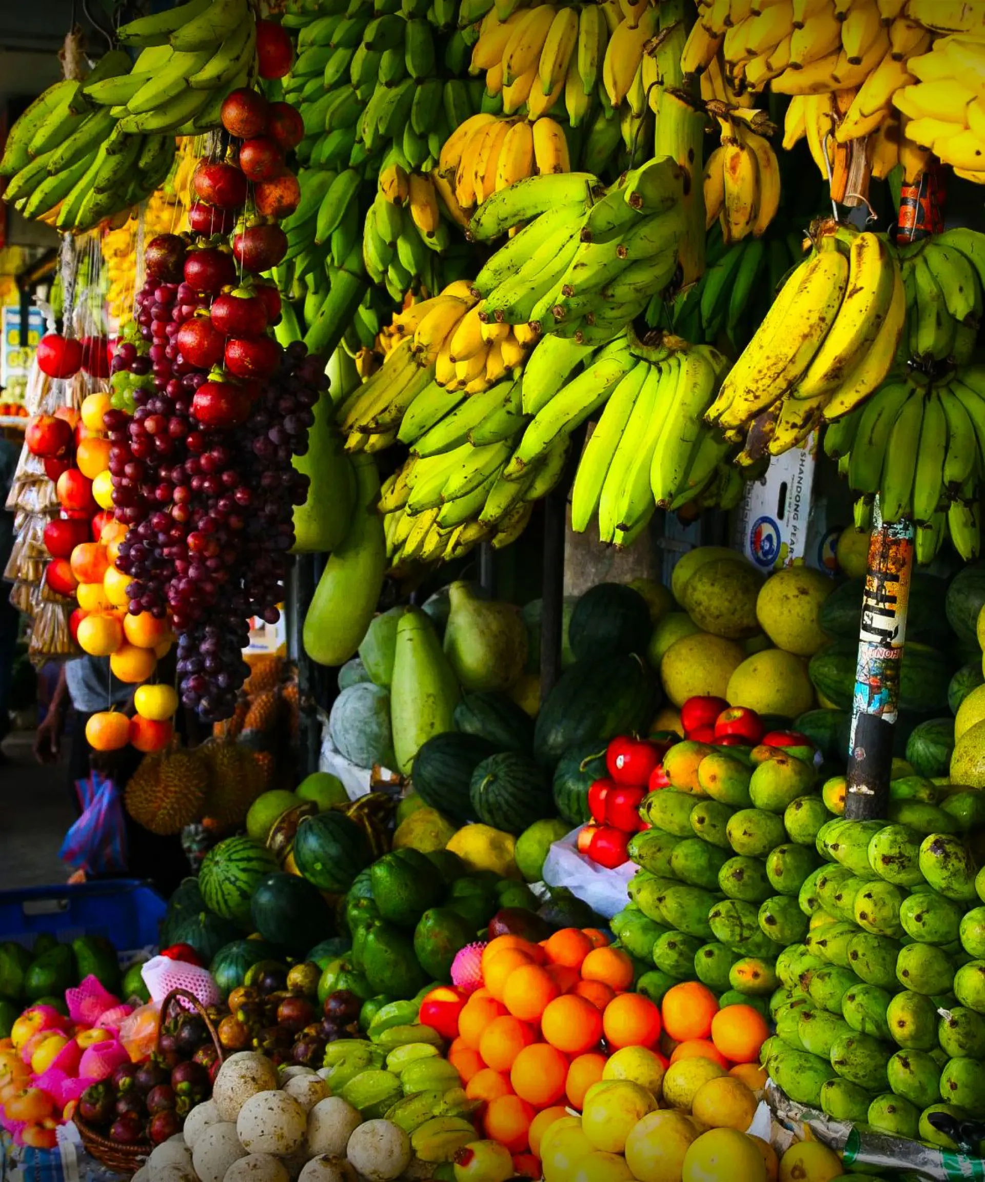 A vibrant fruit market stall with bananas, grapes, and various tropical fruits.